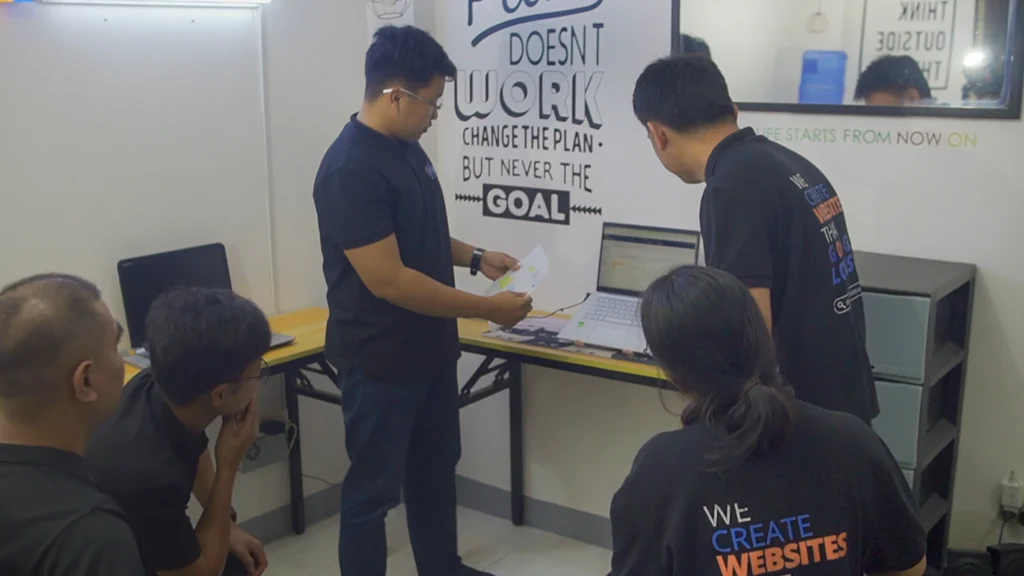 Team members collaborating around a whiteboard while discussing project goals and ideas.
